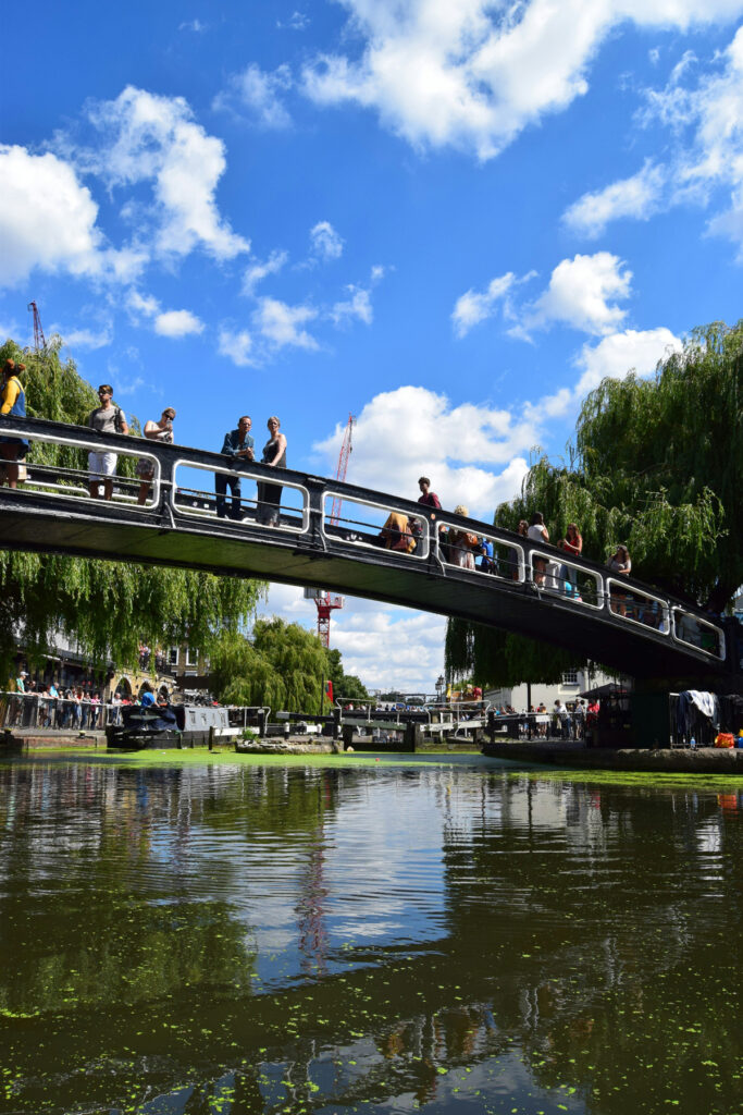people walking across a bridge over a lake on a summer's day