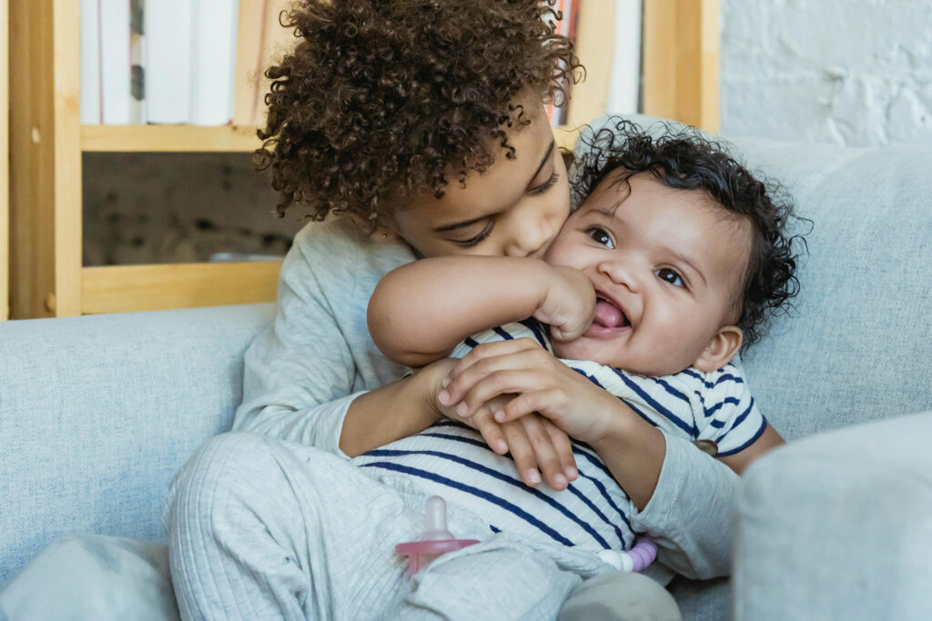 Sibling holding younger baby brother on sofa
