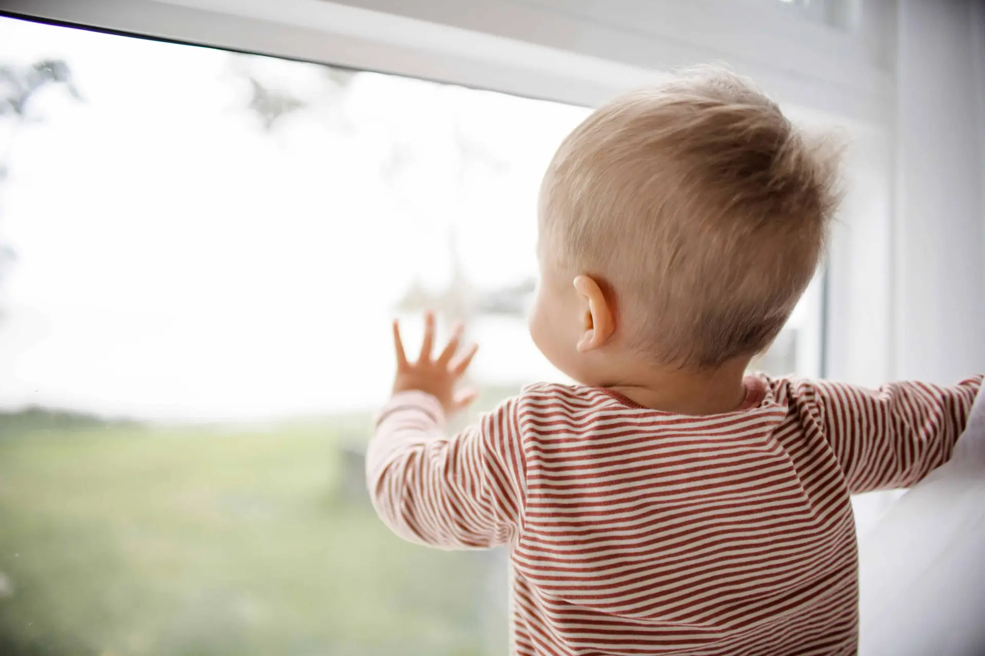 baby looking out window with hand on window