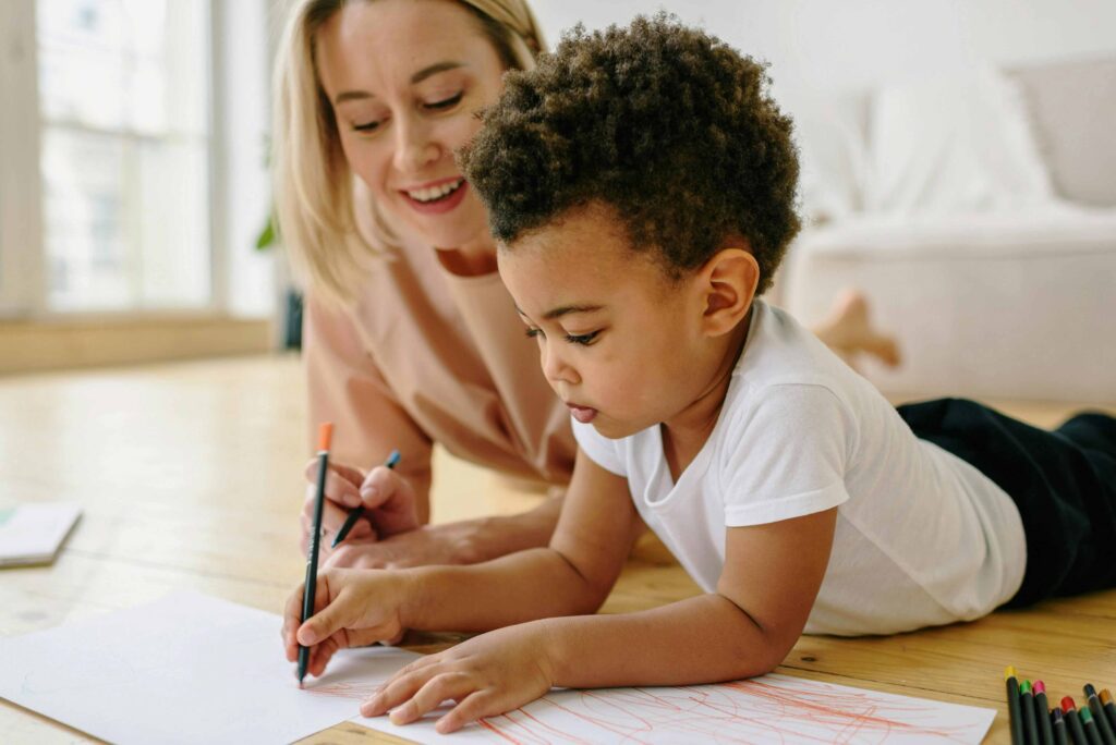 mum and young boy laying on floor with colouring pencils and paper