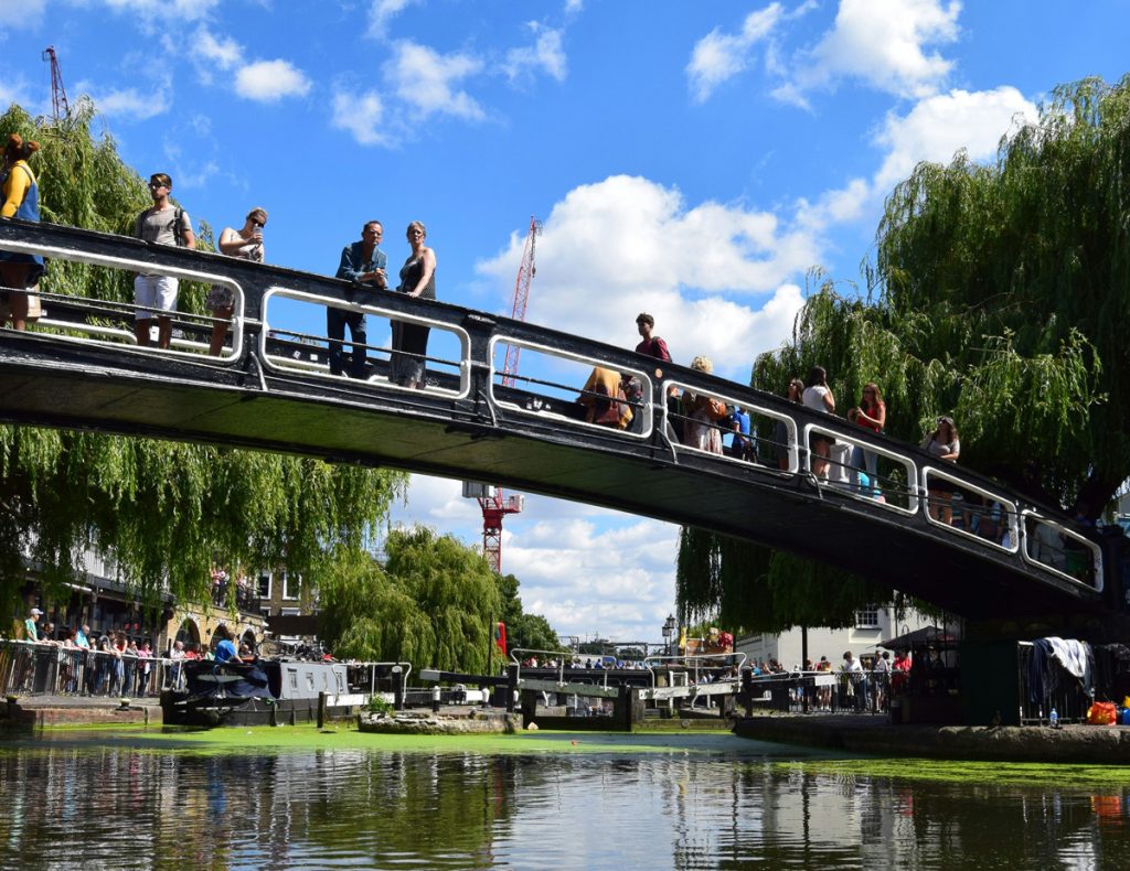 people walking across a bridge over a lake on a summer's day